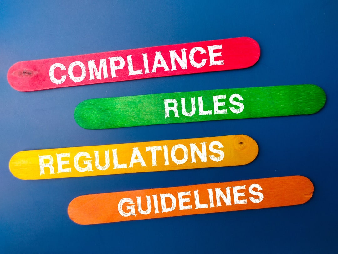 Colored signs with words associated with compliance services: compliance, rules, regulations, and guidelines.