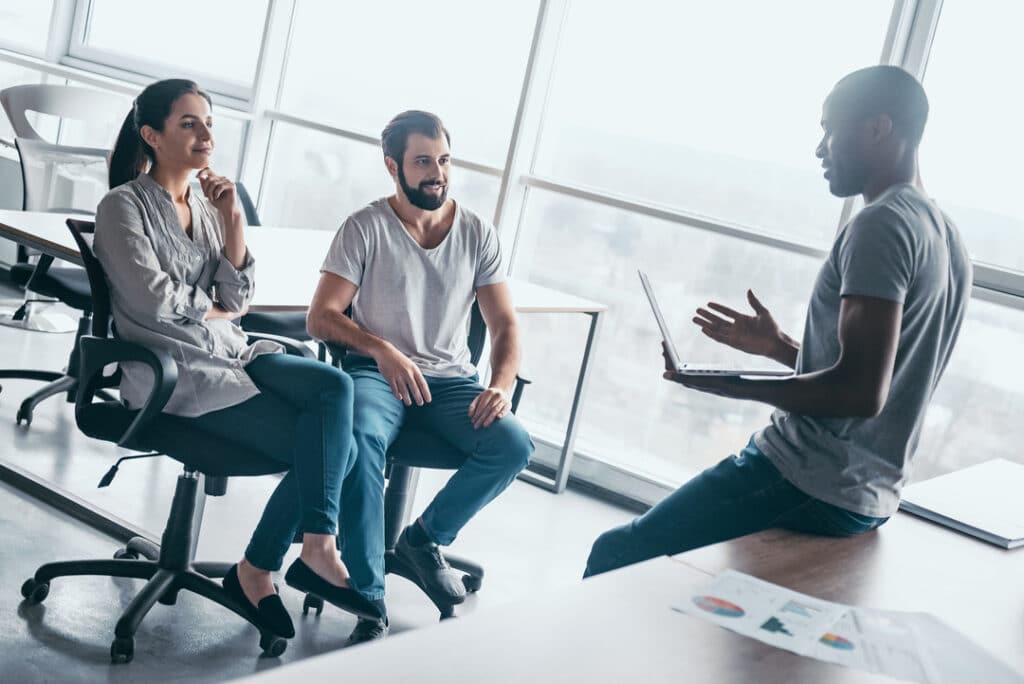 Three coworkers sit in a sunlit office having a business continuity planning meeting.